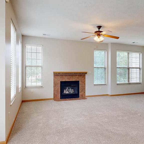 Thumbnail 7 of 39 A living room with a tiled fireplace, several tall windows, and a ceiling fan light.