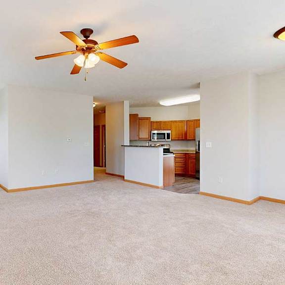 Thumbnail 5 of 39 A living room with a ceiling fan and a kitchen in the background.