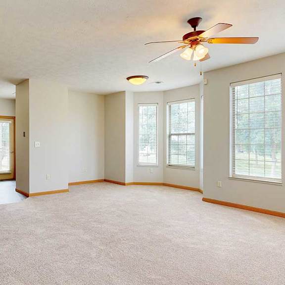 Thumbnail 12 of 39 A spacious living room with a carpeted floor, a bay window in the dining area, a ceiling fan, and a breakfast bar countertop to the kitchen.