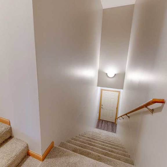 Thumbnail 37 of 39 A carpeted staircase with a wooden handrail leading up from a tiled foyer at the front private entry.