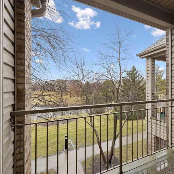 Thumbnail 12 of 23 Covered balcony with metal railing and views of green space and neighboring buildings.