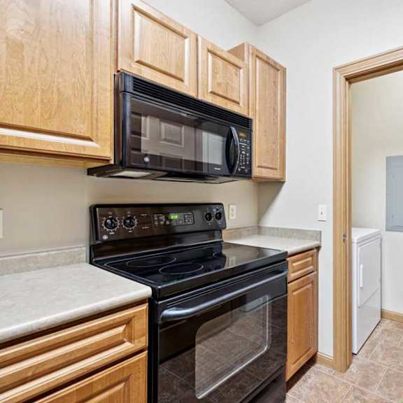 Thumbnail 6 of 23 Kitchen with black refrigerator, oven, and microwave, natural wood cabinets, and tile flooring.