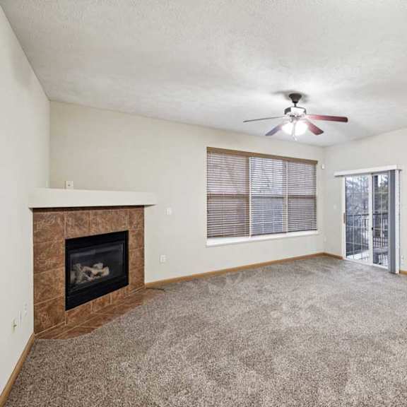 Thumbnail 11 of 23 Spacious living room with plush carpet, ceiling fan, corner fireplace, and sliding glass door to balcony.