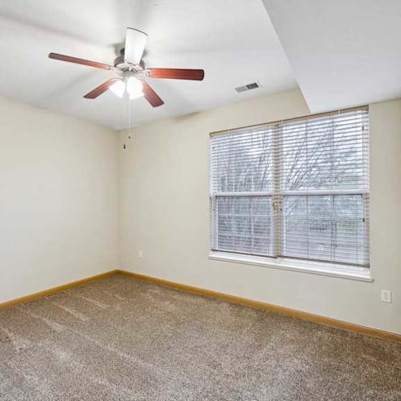 Thumbnail 15 of 19 Bright bedroom with plush carpet, neutral walls, ceiling fan with light, and large window with blinds.