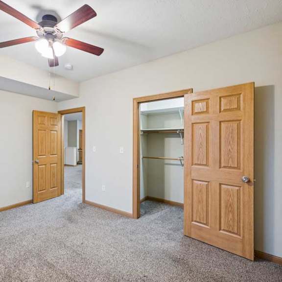 Thumbnail 16 of 19 Carpeted bedroom featuring ceiling fan, double-door closet, and natural wood trim throughout the apartment interior.
