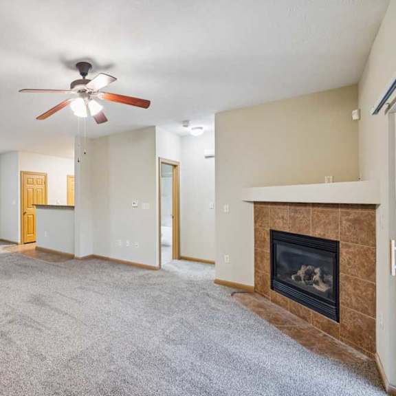 Thumbnail 8 of 19 Spacious living room with plush carpet, ceiling fan, tile-surround fireplace, and open layout to kitchen.