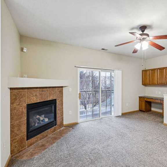 Thumbnail 4 of 19 Living room with corner fireplace, ceiling fan, and built-in desk nook near balcony access.