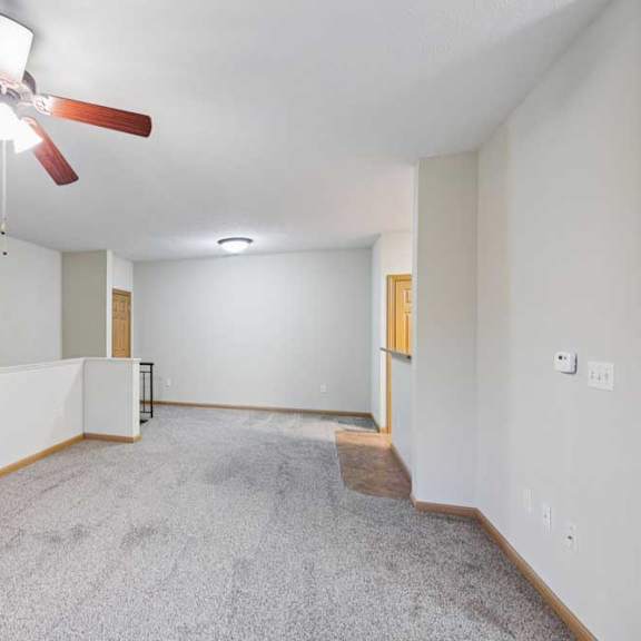 Thumbnail 9 of 19 Spacious living area with plush carpet, neutral walls, ceiling fan, and half wall overlooking stairs