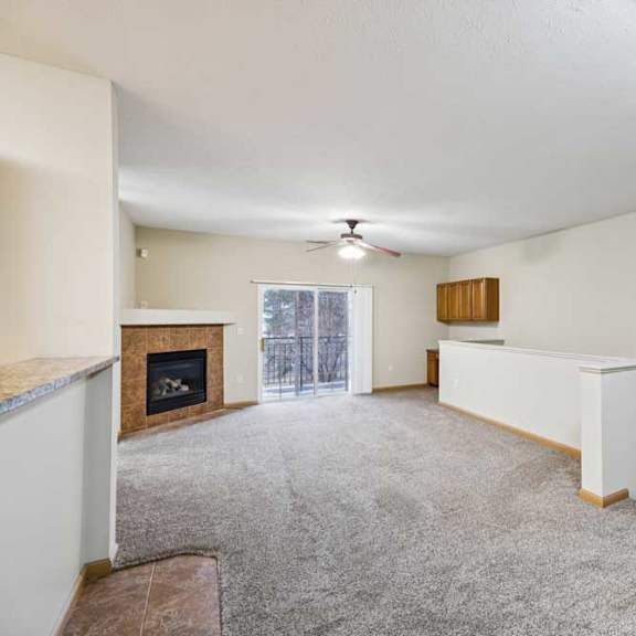 Thumbnail 3 of 19 Open-concept apartment living room with tile-surround fireplace, sliding glass door to balcony, and stair railing leading downstairs.
