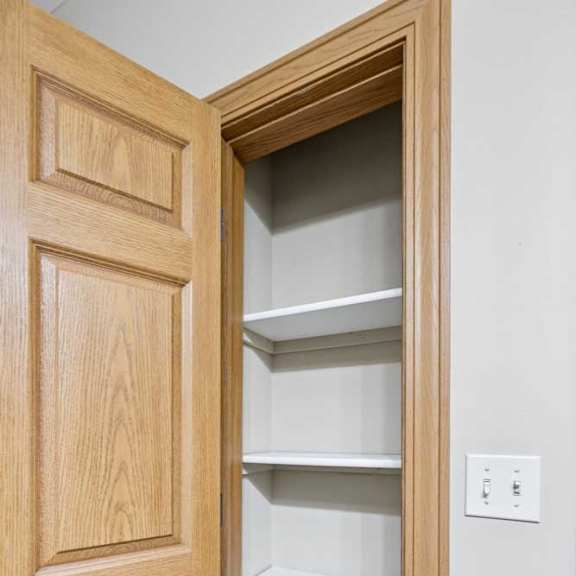 Thumbnail 18 of 19 Linen closet with built-in white shelving and wood trim, offering convenient storage space inside the apartment.