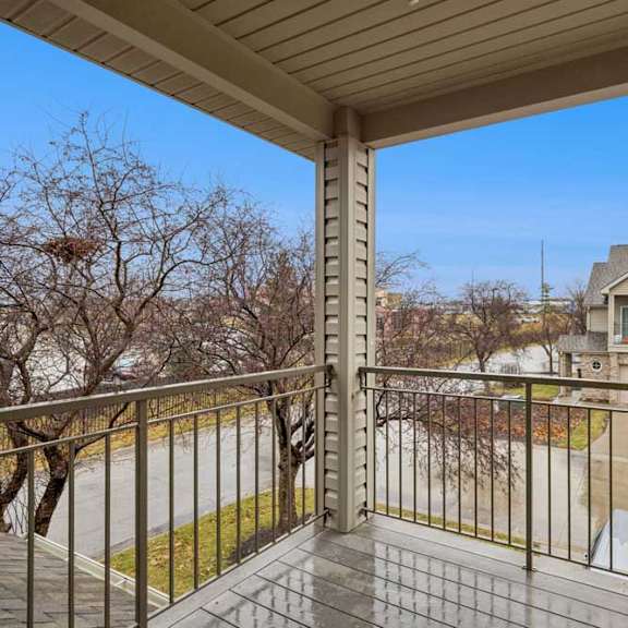 Thumbnail 12 of 19 Covered upper-level balcony with wood-look flooring, metal railing, and neighborhood views.