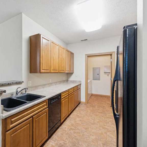 Thumbnail 5 of 19 Kitchen with natural wood cabinets, laminate countertops, double-basin sink, black dishwasher, and adjacent laundry room access.