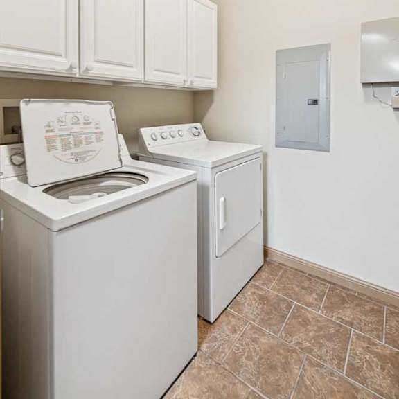 Thumbnail 7 of 19 In-unit laundry room with washer and dryer, white upper cabinets, and tile flooring.