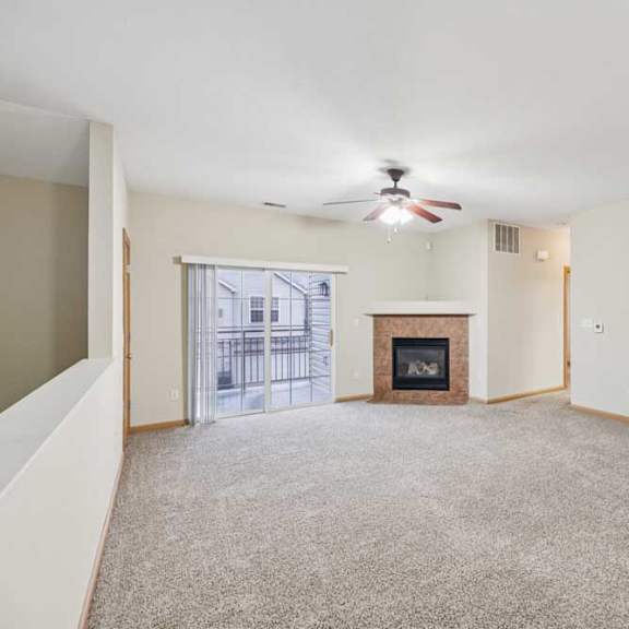 Thumbnail 9 of 19 Open living room with plush carpet, ceiling fan, sliding glass door to private balcony, and corner fireplace with tile surround.