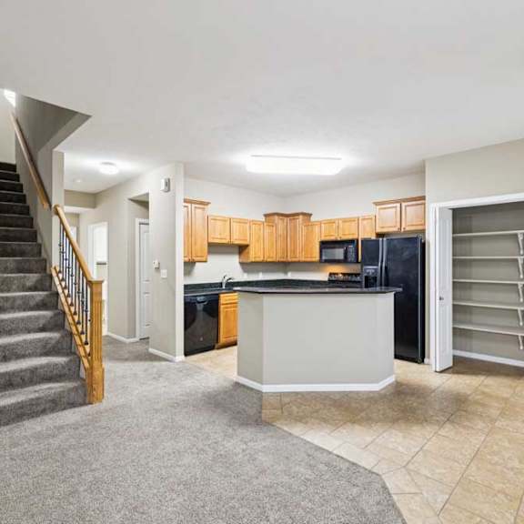 Thumbnail 13 of 26 Open-concept apartment living area with carpeted stairs, tile kitchen flooring, peninsula breakfast bar, and walk-in pantry with built-in shelving.