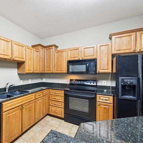 Thumbnail 3 of 26 U-shaped kitchen with natural wood cabinets, black granite countertops, black appliances, and double-basin sink.