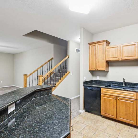 Thumbnail 5 of 26 Kitchen and stair view showcasing granite counters, dishwasher, and open layout to living space.