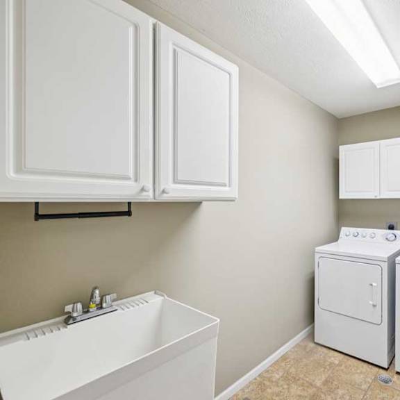 Thumbnail 7 of 26 In-unit laundry room with washer and dryer, utility sink, and overhead storage cabinets.
