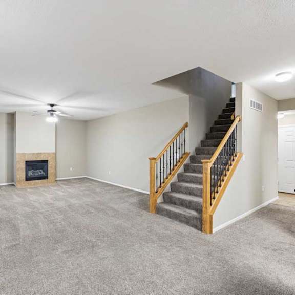 Thumbnail 10 of 26 Spacious living room with plush carpet, staircase with wood railing, and gas fireplace.