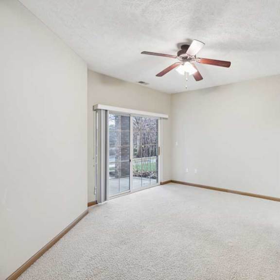 Thumbnail 13 of 20 Spacious bedroom with plush carpet, ceiling fan, and sliding glass door leading to a private patio.