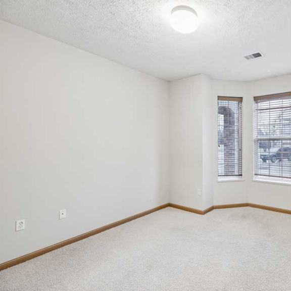 Thumbnail 18 of 20 Bright bedroom with bay-style windows, neutral carpet, and wood trim for a clean apartment interior.