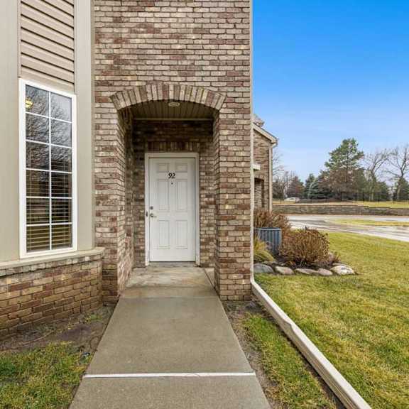 Thumbnail 2 of 20 Brick apartment townhome exterior with covered arched entry, private front door, and landscaped lawn.