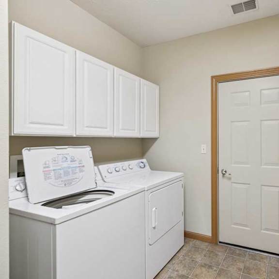 Thumbnail 11 of 20 Laundry room with full-size washer and dryer, upper storage cabinets, and tile-look flooring.