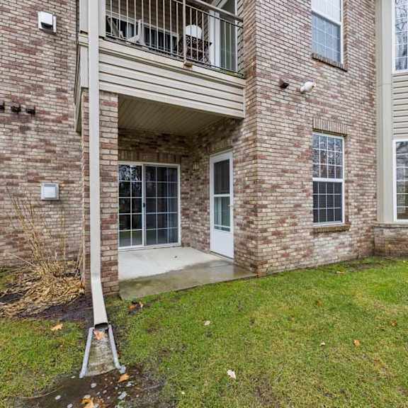 Thumbnail 14 of 20 Brick apartment exterior with ground-level patio, sliding glass door entry, and upper balcony.