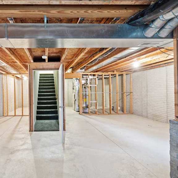 Thumbnail 24 of 25 Unfinished duplex basement with exposed ceiling joists, concrete floors, utility area, and staircase access to main level.