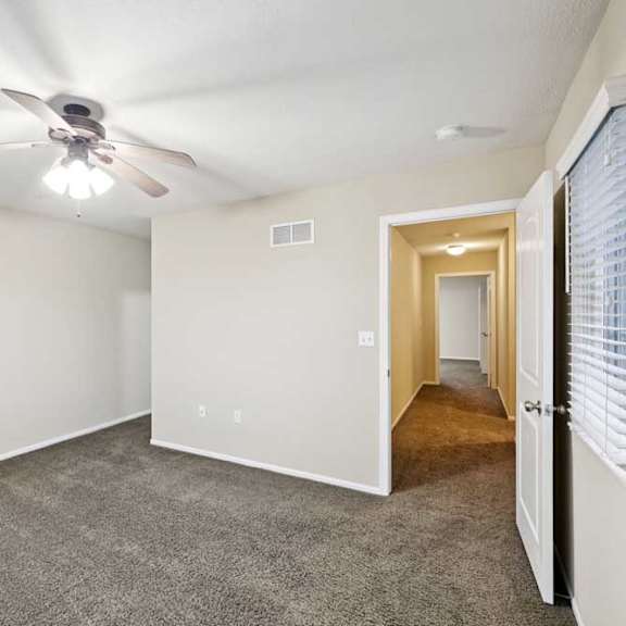 Thumbnail 17 of 25 Spacious bedroom with plush carpet, ceiling fan, and hallway access.