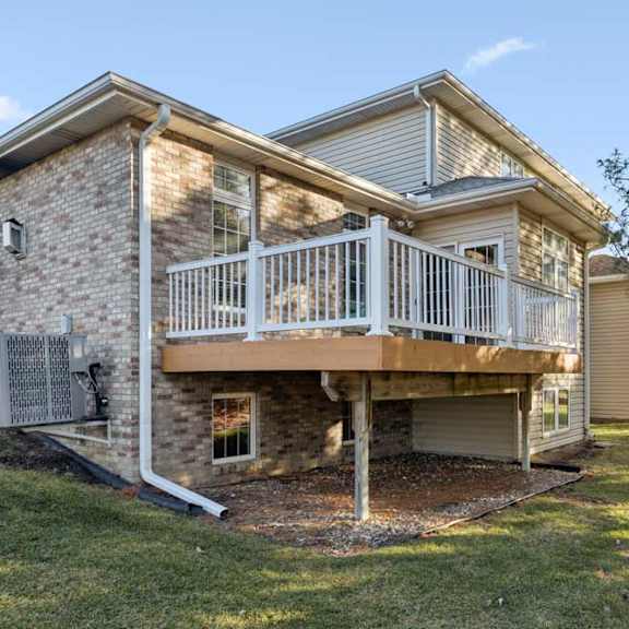 rear duplex exterior with elevated deck, white railing, brick and siding facade, and backyard lawn.