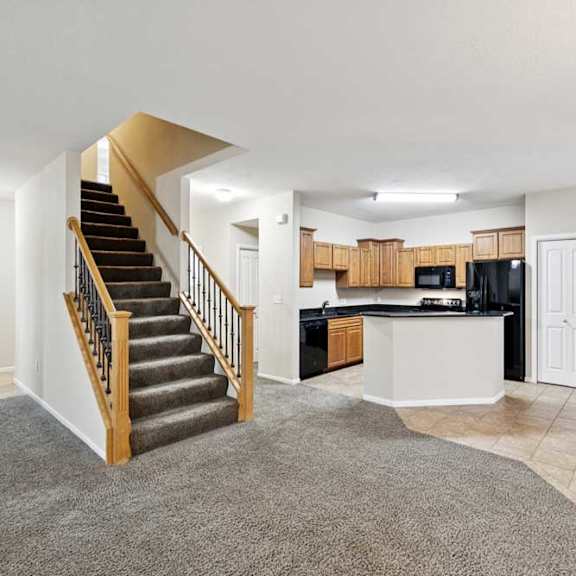 open-concept living space with staircase, carpet and tile flooring, and kitchen with peninsula seating.