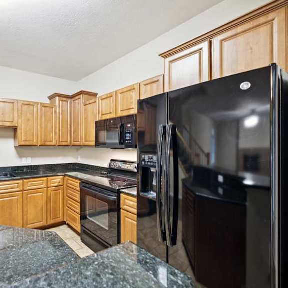 Thumbnail 9 of 25 Kitchen with natural wood cabinets, black appliances, granite countertops, and peninsula with bar seating.
