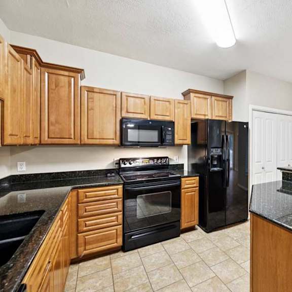 Thumbnail 11 of 25 Kitchen with granite peninsula, black refrigerator, pantry closet, and adjacent dining area with large window.