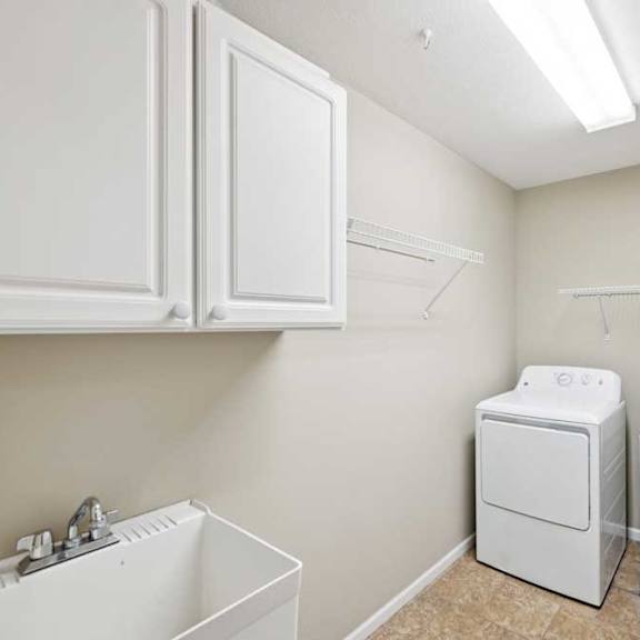 Thumbnail 14 of 25 Laundry room with utility sink, washer and dryer, upper cabinets, and wire shelving.