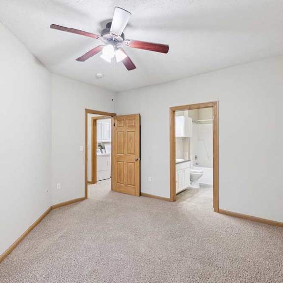 Thumbnail 14 of 21 Primary bedroom with neutral walls, ceiling fan, and en-suite bath and laundry access.