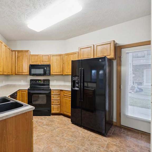kitchen with natural wood cabinets, black appliances, double-basin sink, and door to private balcony.