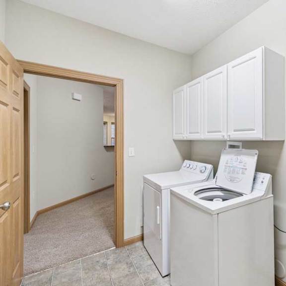 laundry area with overhead cabinetry, adjacent utility closet, and doorway to carpeted living space.