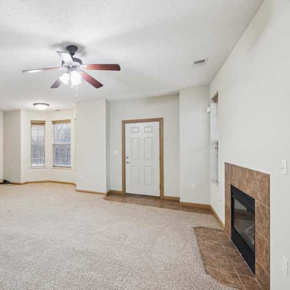 spacious open living room with plush carpet, ceiling fan, tiled entry, and corner gas fireplace.