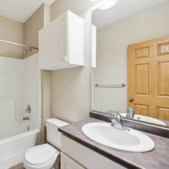 Thumbnail 21 of 21 Apartment bathroom with tub and shower combination, single-sink vanity, wall cabinet, and wood trim accents.
