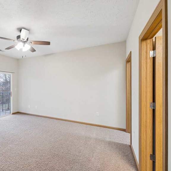 Thumbnail 4 of 21 Spacious apartment living room with neutral carpet, ceiling fan, and sliding glass door leading to a private balcony with outdoor views.