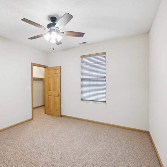 Thumbnail 17 of 21 Empty bedroom with neutral carpet, ceiling fan, wood trim, and open doorway to an attached closet.