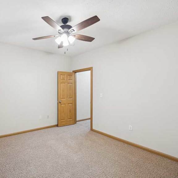 Thumbnail 20 of 21 Bright, empty apartment bedroom with neutral carpet, white walls, wood trim, a ceiling fan with light, and a large window with blinds for natural light.