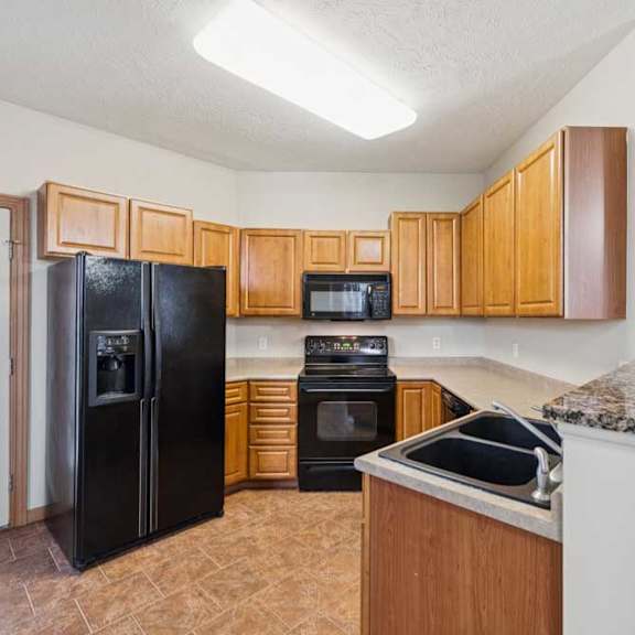 Thumbnail 12 of 21 U-shaped apartment kitchen with wood cabinetry, black appliances, oven with over-the-range microwave, double-basin sink, and laminate countertops.