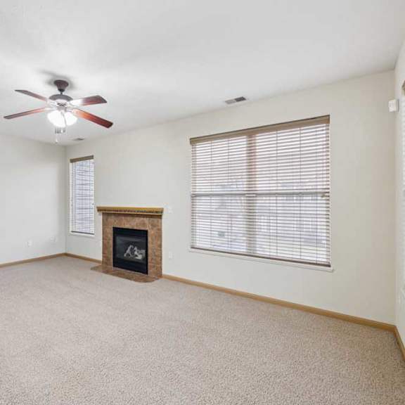 Thumbnail 11 of 21 Open living area with large windows, neutral carpet, and a corner fireplace with tile surround and wood mantel for added warmth.