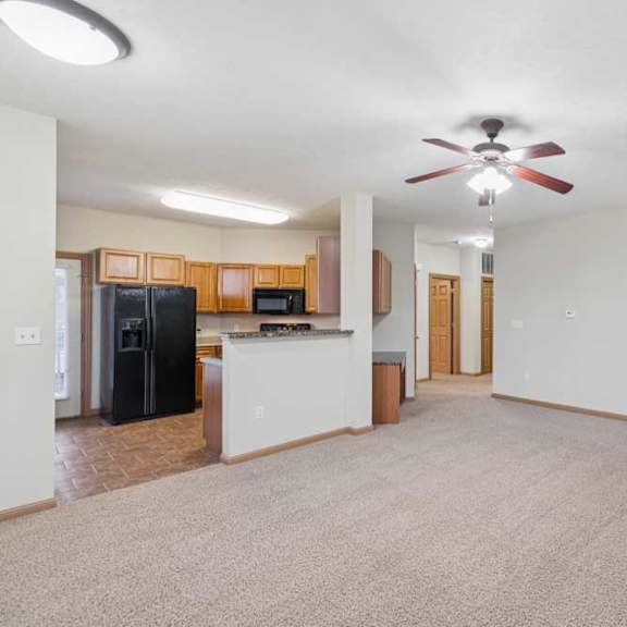 Thumbnail 16 of 21 Open-concept living room with neutral carpet, ceiling fan, corner fireplace with tile surround, and view into the adjoining kitchen.