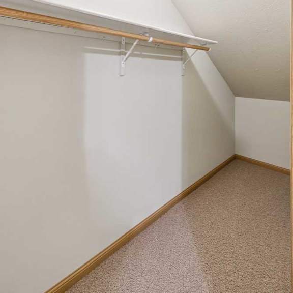 Thumbnail 18 of 21 Under-stair storage space with sloped ceiling, carpet flooring, hanging rod, and built-in shelf for organized storage.