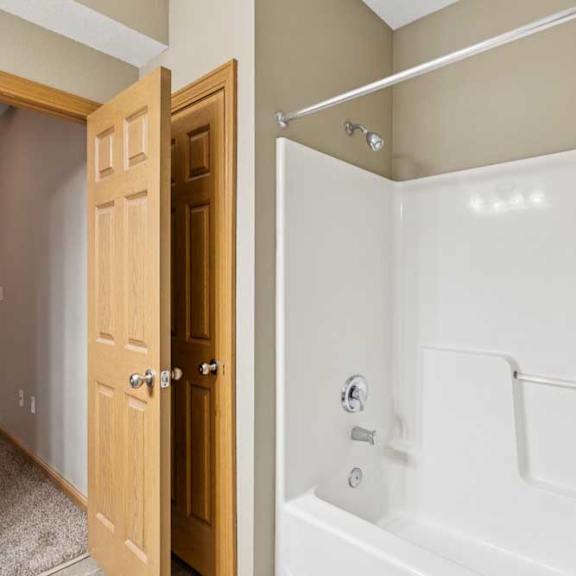 Thumbnail 18 of 20 Tub and shower combination with built-in surround, towel bar, and wood-trimmed door leading to the hallway.