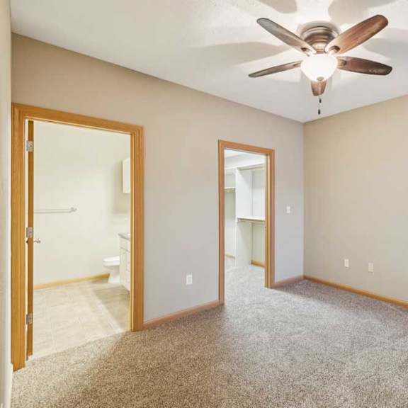 Thumbnail 13 of 20 Carpeted bedroom with ceiling fan, en-suite bathroom access, and doorway to a walk-in closet.