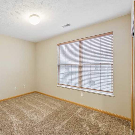 Thumbnail 19 of 20 Bright bedroom with large window and blinds, neutral carpet, and wood trim for a clean, updated apartment interior.